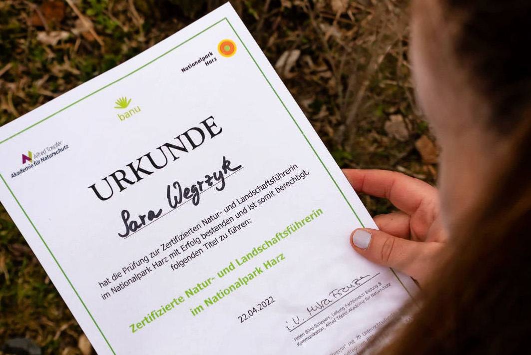 she wanders: Sara hält das Zertifikat zum Nationalpark Harz Guide in den Händen.